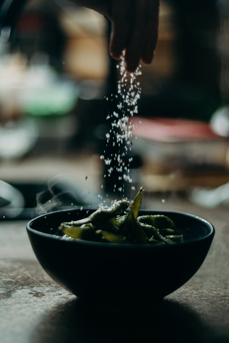 a person sprinkling salt on a bowl of food