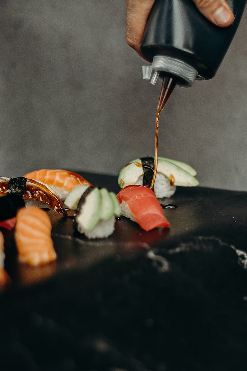 a person pouring sauce over sushi on a table